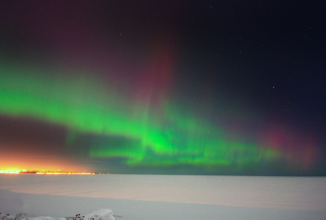 Northern lights dancing over a frozen Lake Superior while the lights ofMarquette twinkle in the distance