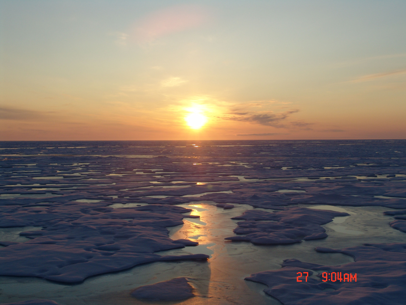 An amber sun reflecting off ice floes and melt pools