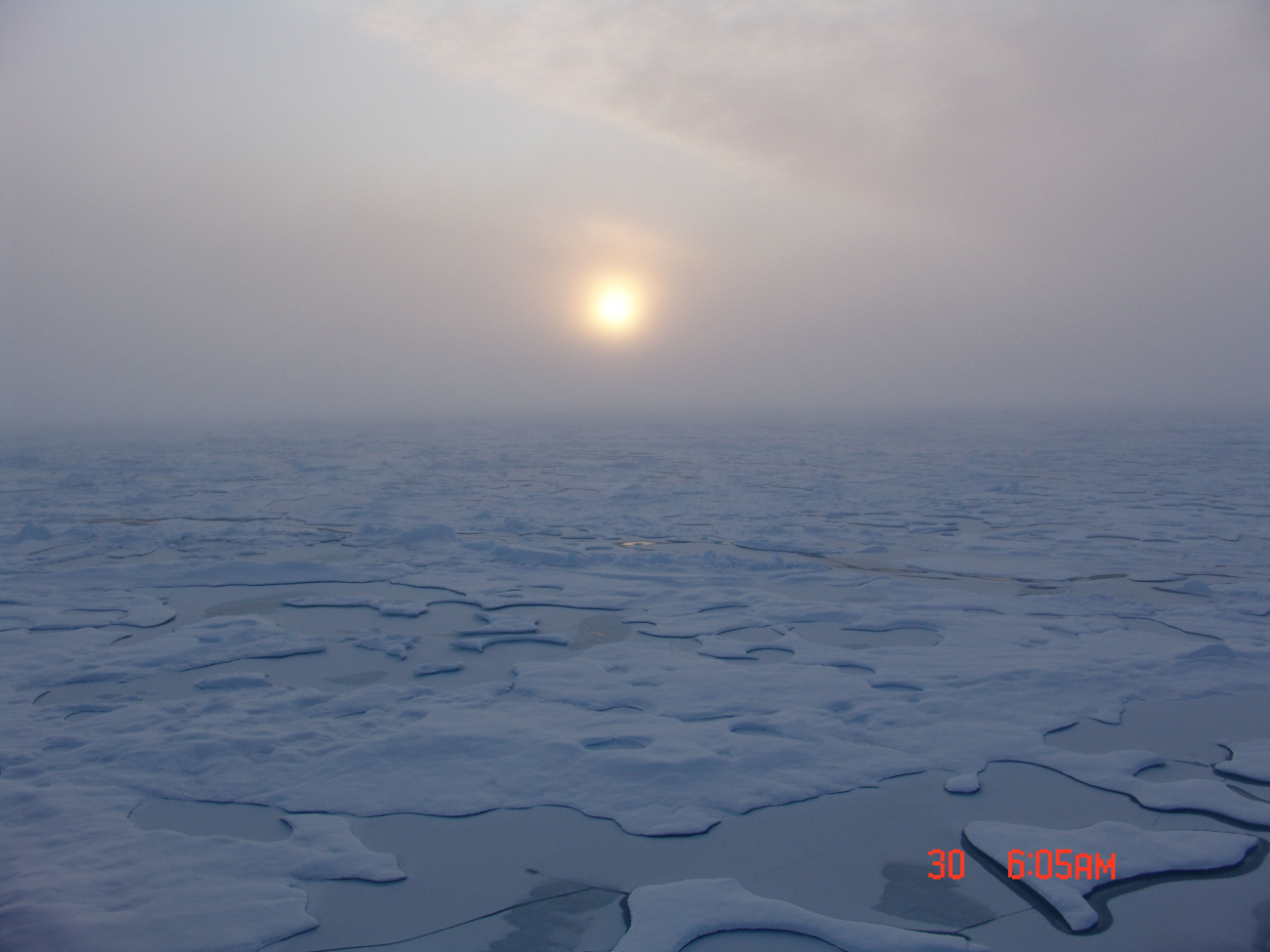 Sun seen through the clouds seen over ice floes and melt ponds