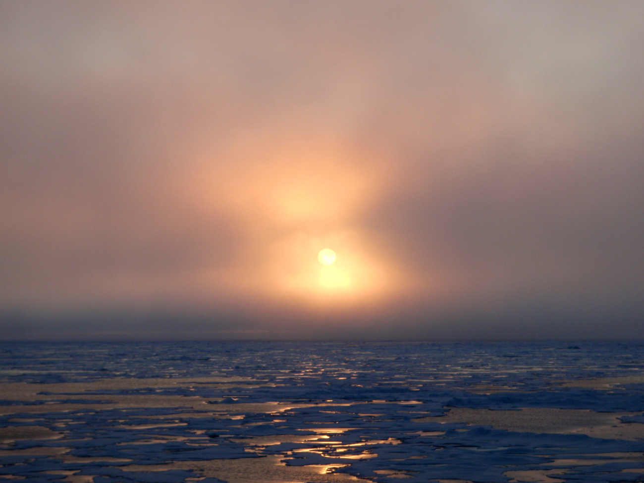 Sun seen through the clouds over late summer ice floes