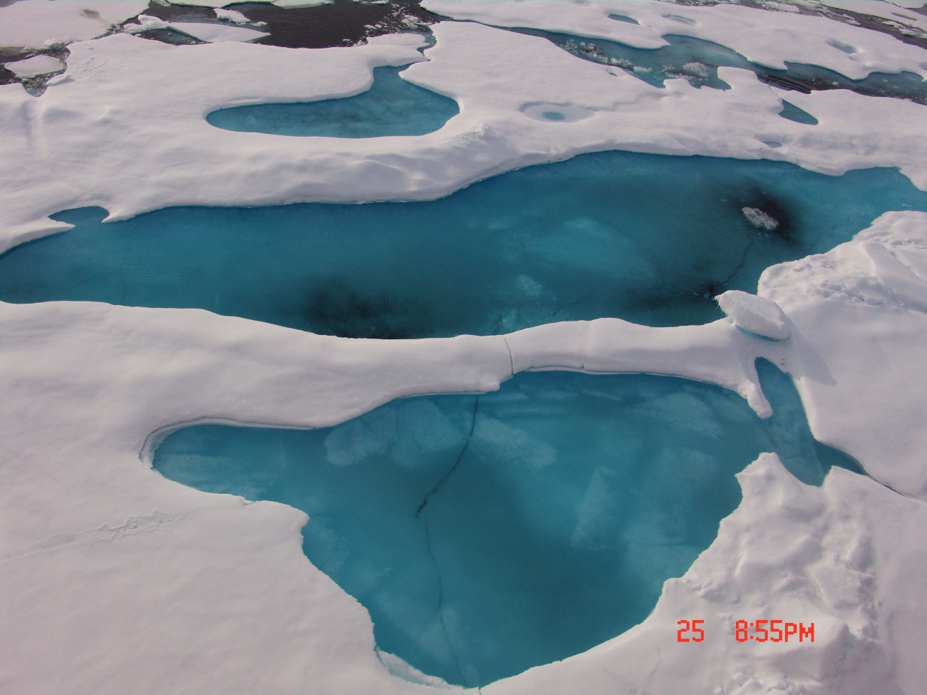 Looking down to aquamarine colored ice with melt ponds melting through tounderlying seawater