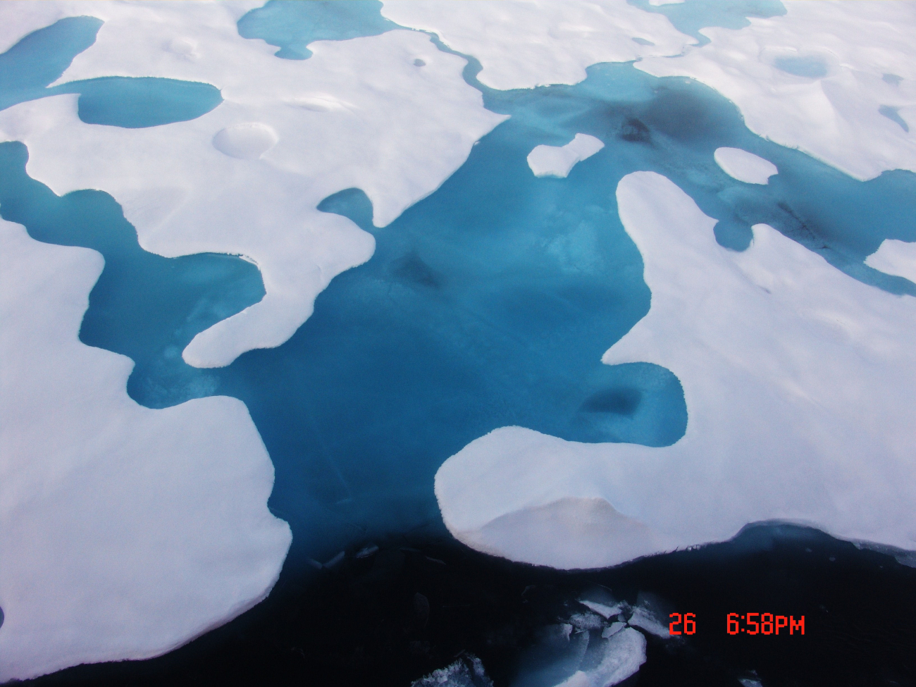 Melt pools breaking through with the dark area at bottom being Arctic seawater
