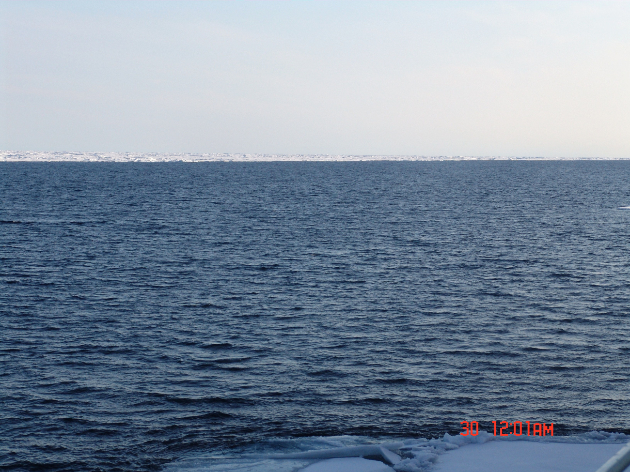 A large area of open water with unbroken ice pack in the distance