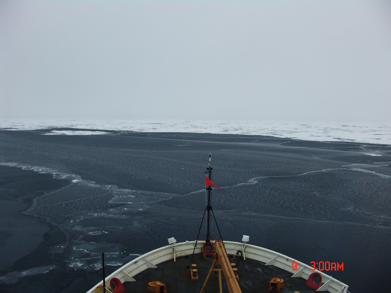 The bow of the CGC HEALY is seen as it breaks through dark nilas ice