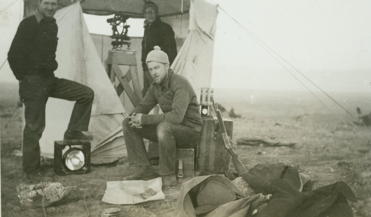 Bill Husemeyer at the theodolite and Vic Smith sitting on instrument bow at astation along the 46th Parallel in Montana
