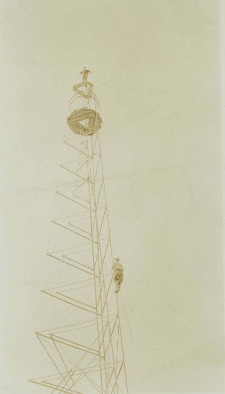 Floyd Risvold standing on top of 110-foot tower with Bill Kessler climbing upthe ladder leg at Station Livingston