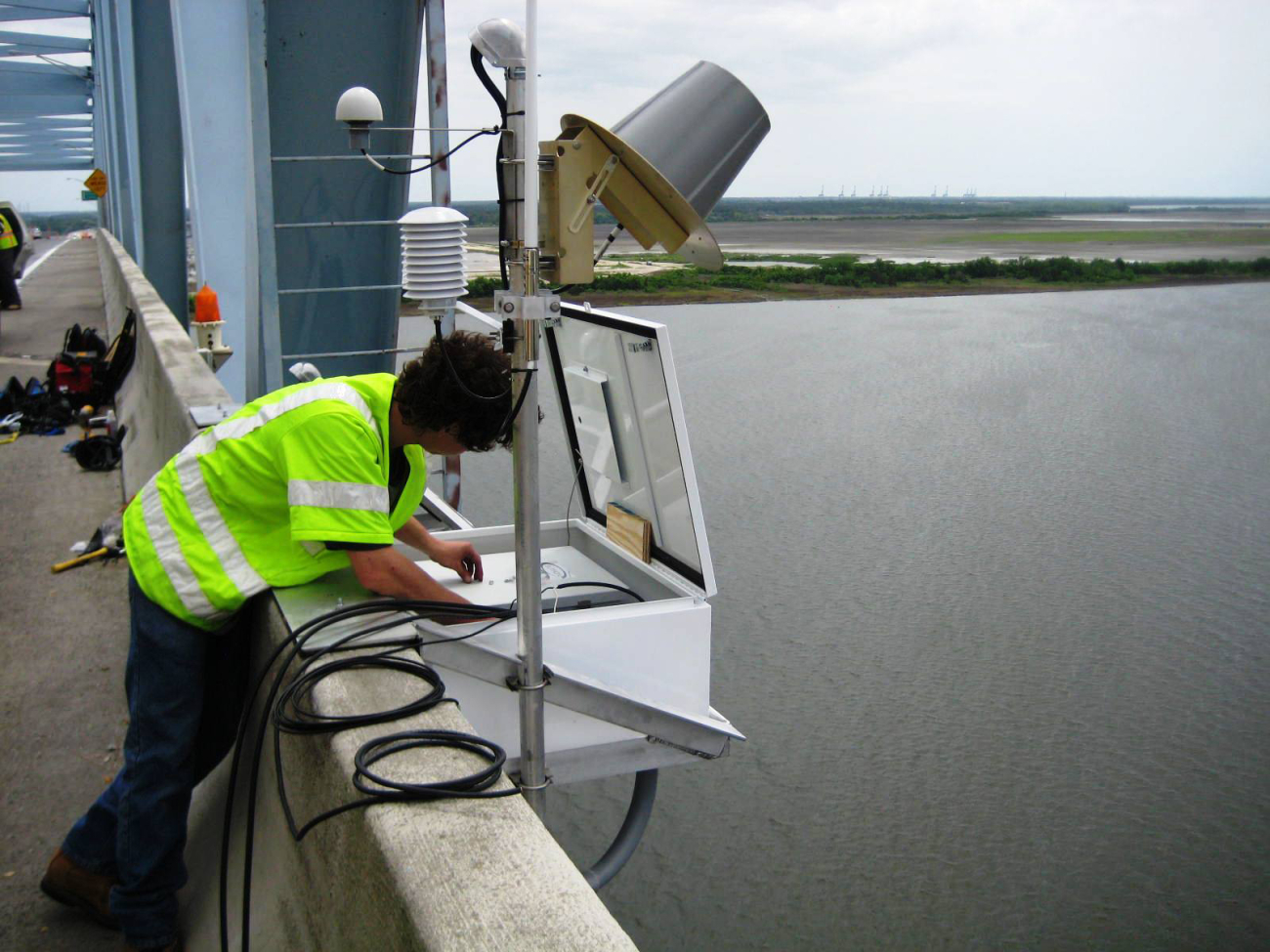 An employee of NOAA's Center for Operational Oceanographic Products (CO-OPS)installs an air gap sensor on the Don Holt Bridge