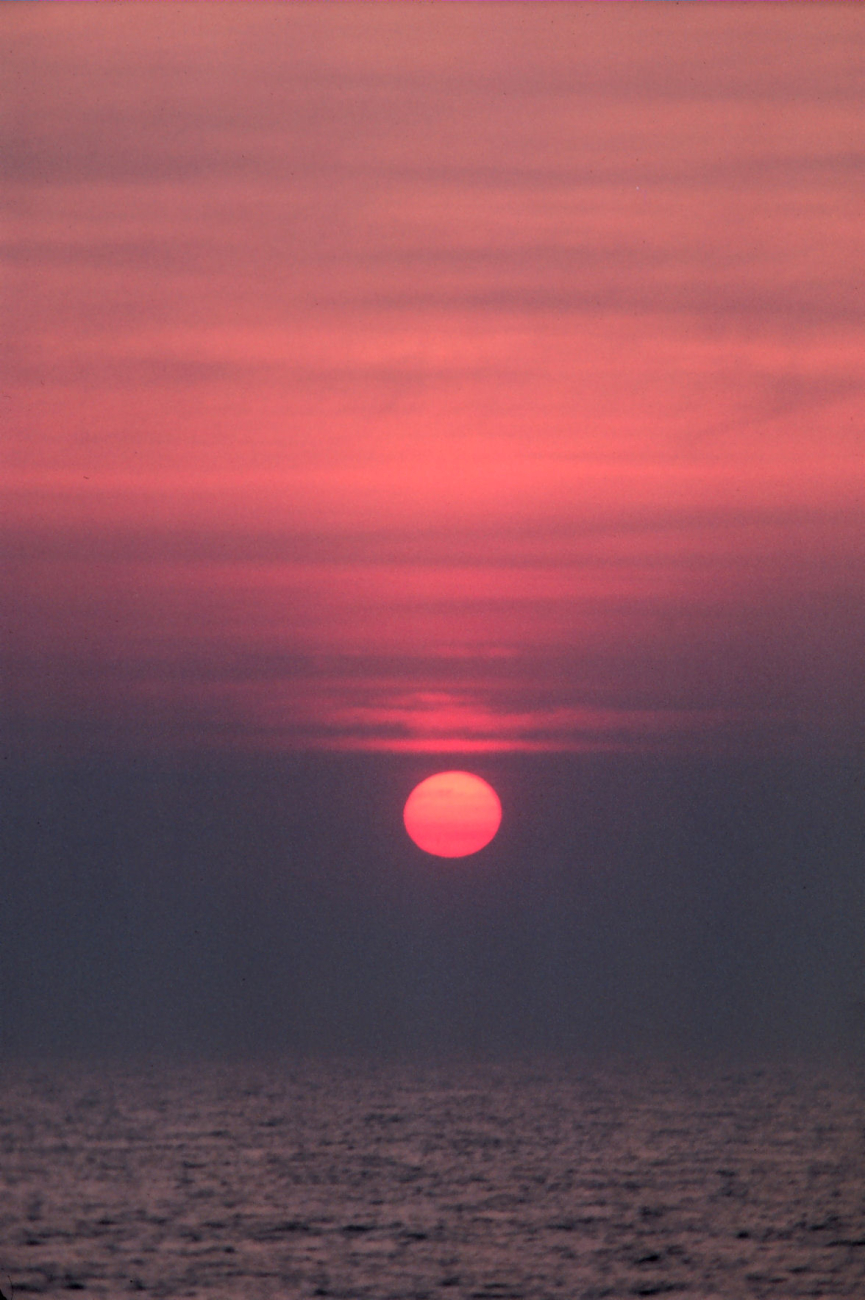 Sun as an orange sphere setting over the ocean