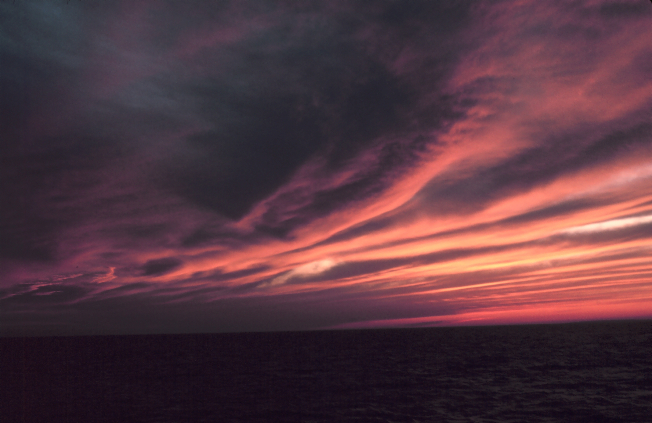 Parallel cloud bands illuminated by sun setting over the ocean