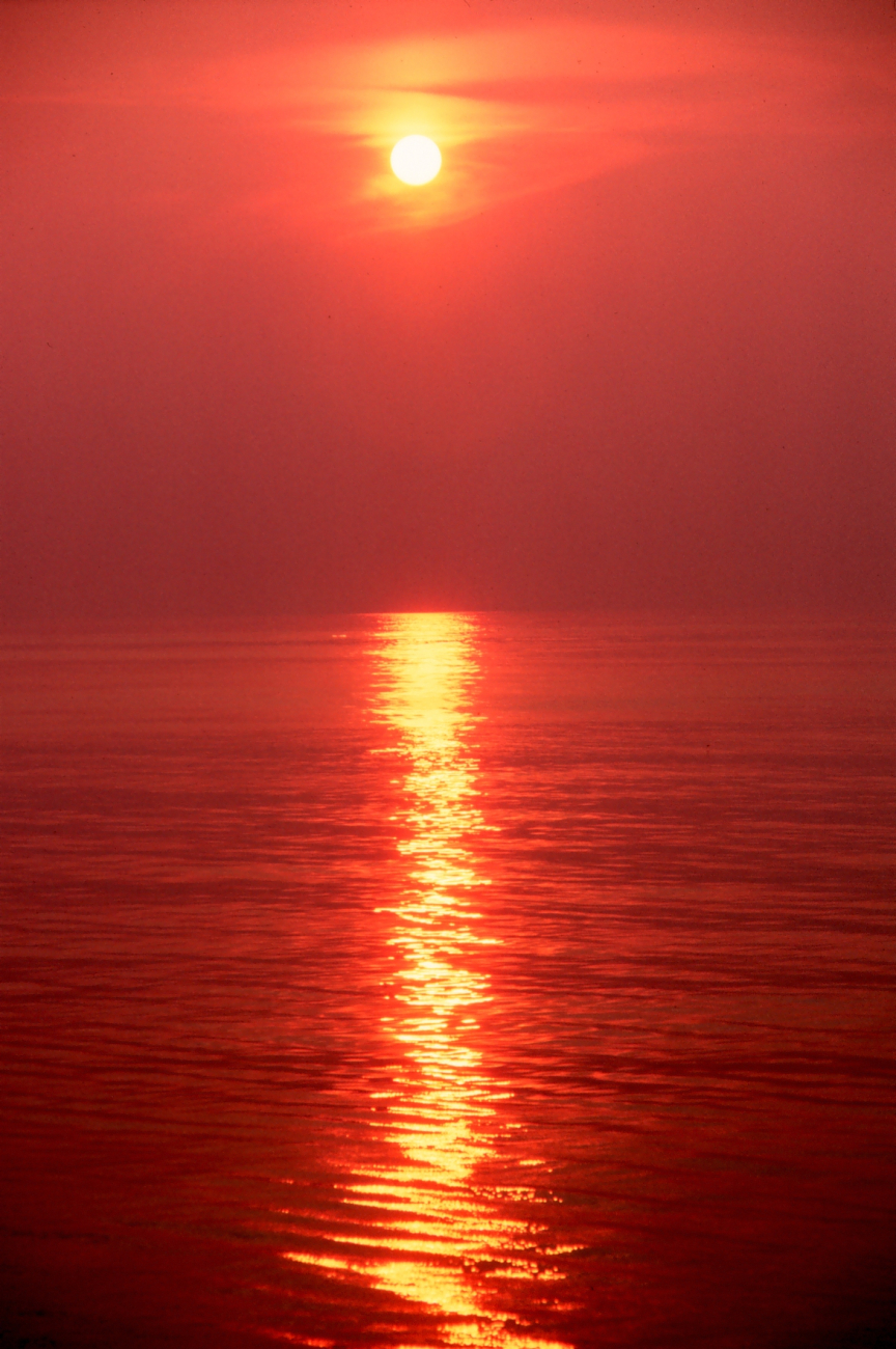 Orange sky and orange sea with a pillar of light reflecting off the ocean
