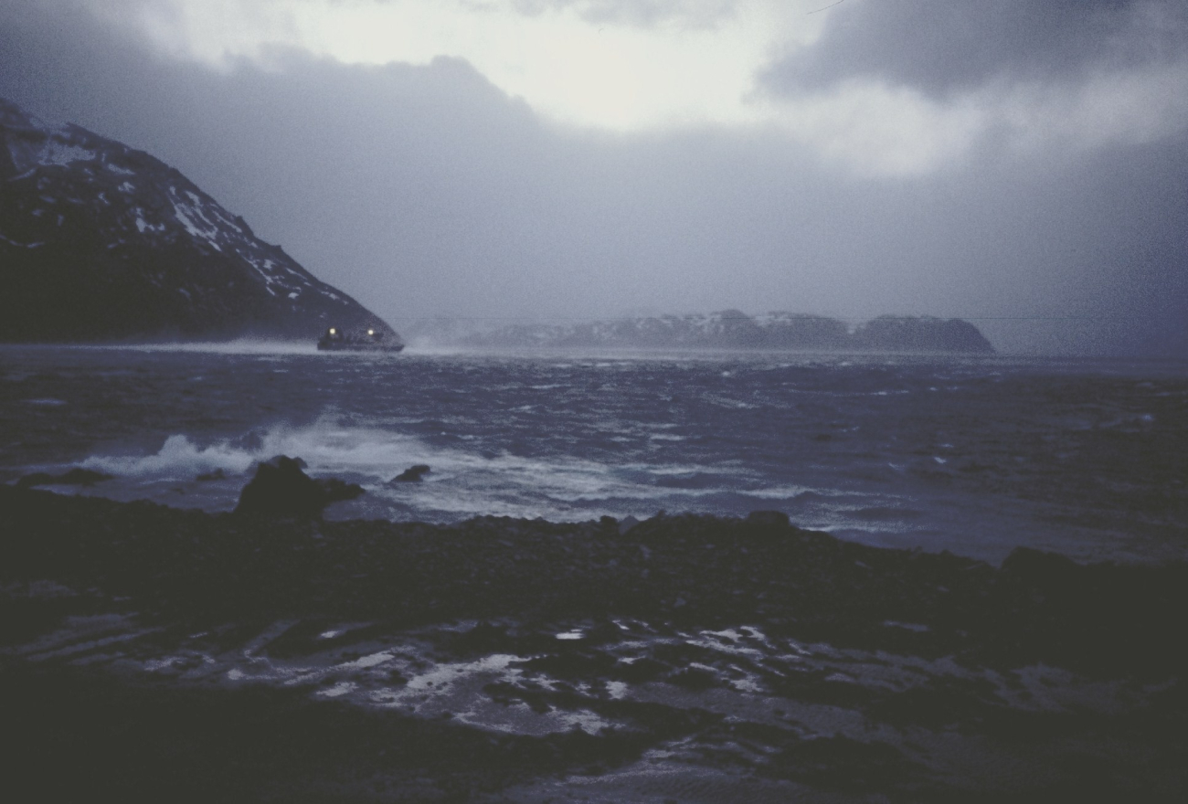 A large fishing vessel leaving Dutch Harbor on a gray, cold, windy evening
