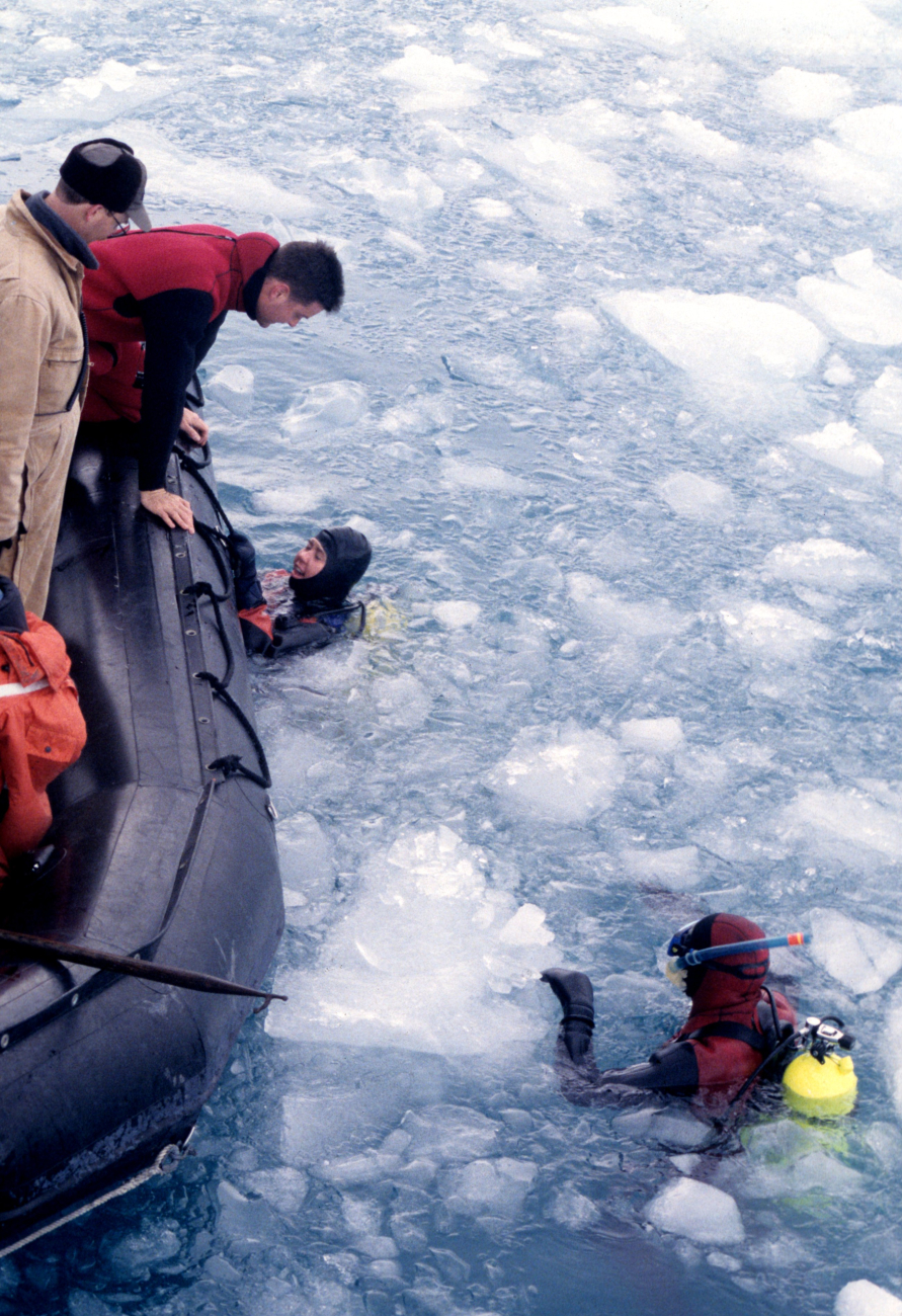 A pair of SCUBA divers look to climb out of the icy water and backaboard the Zodiac