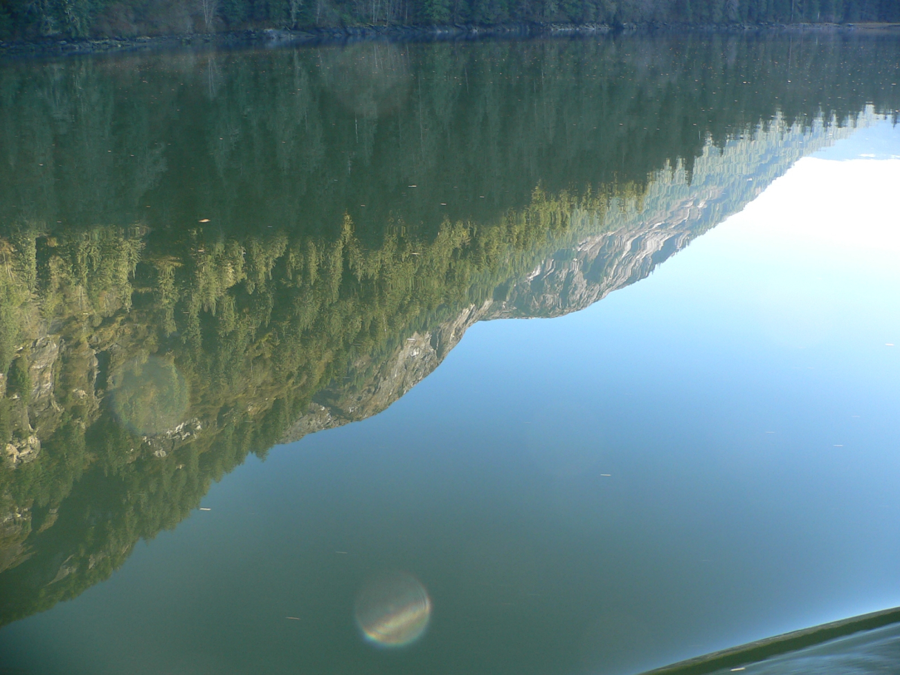 A mirror-like reflection of mountains and trees on a placid inlet