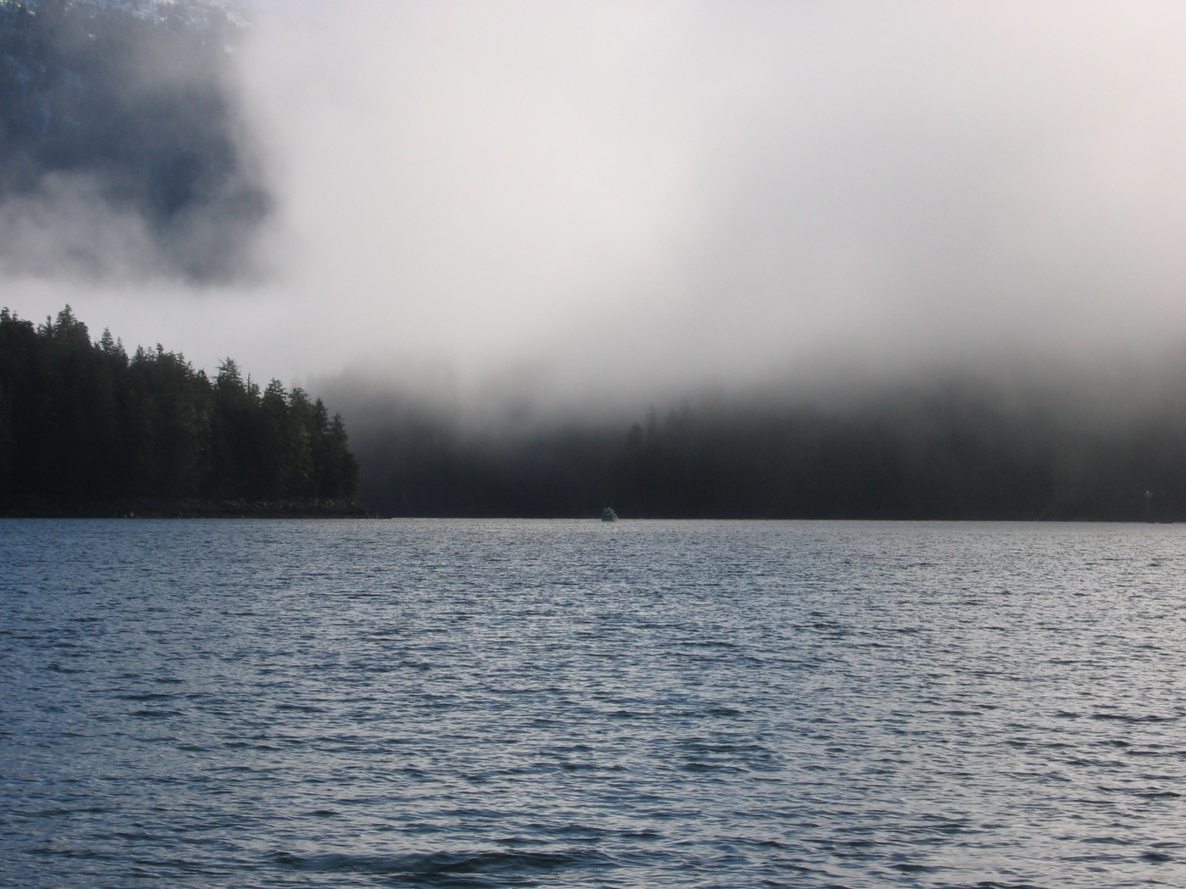 A sounding boat is seen in the distance below fog shrouded hills