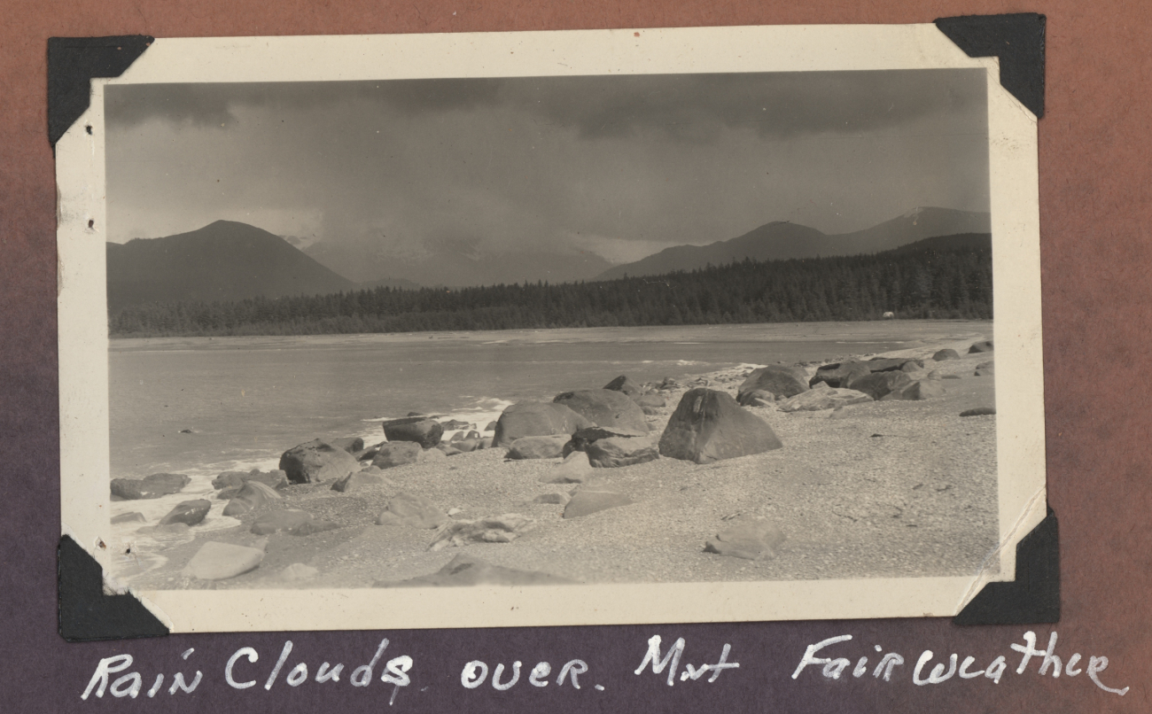 Looking over a sand and boulder beach to Mount Fairweather enveloped inrain clouds