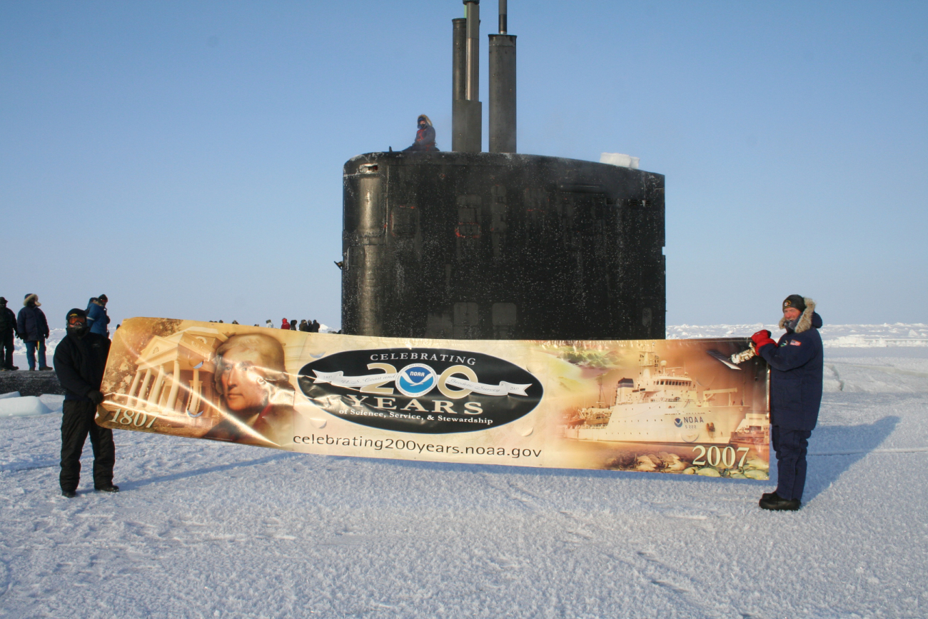 Commander Mike Bernacchi (right), commanding officer of the nuclear-poweredattack submarine USS Alexandria, and a shipmate join NOAA's 200th celebrationfrom atop the world, after the submarine sail broke through the ice at the North Pole