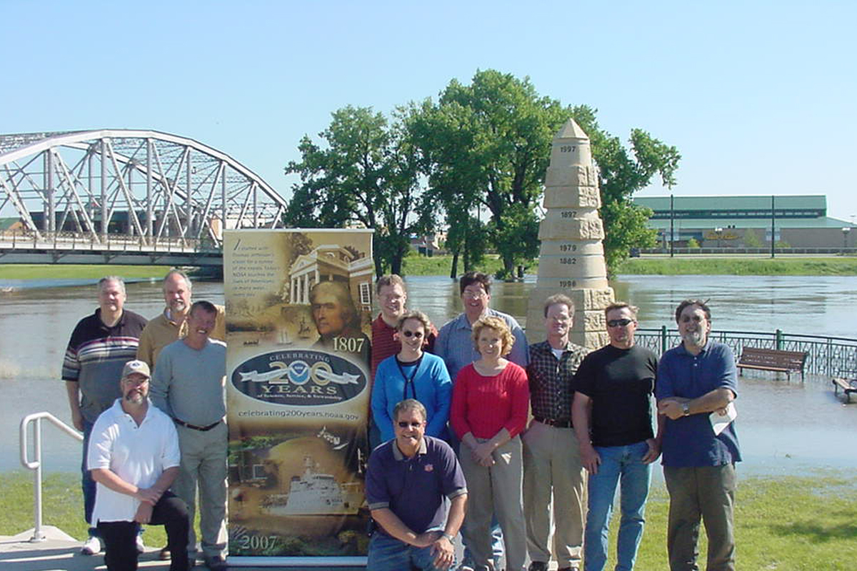 Staff of the NOAA Weather Forecast Office in Grand  Forks celebrating NOAA's 200years of science and service along the banks of the Red River of the North, atthe height of its recent summer crest