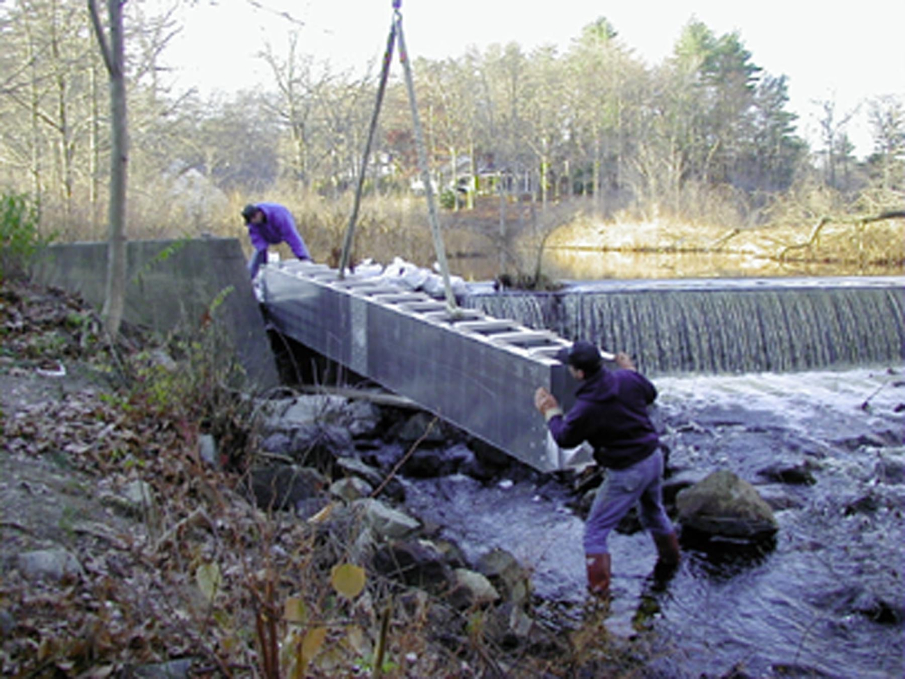 Two workers guide the first section of the fish ladder into place