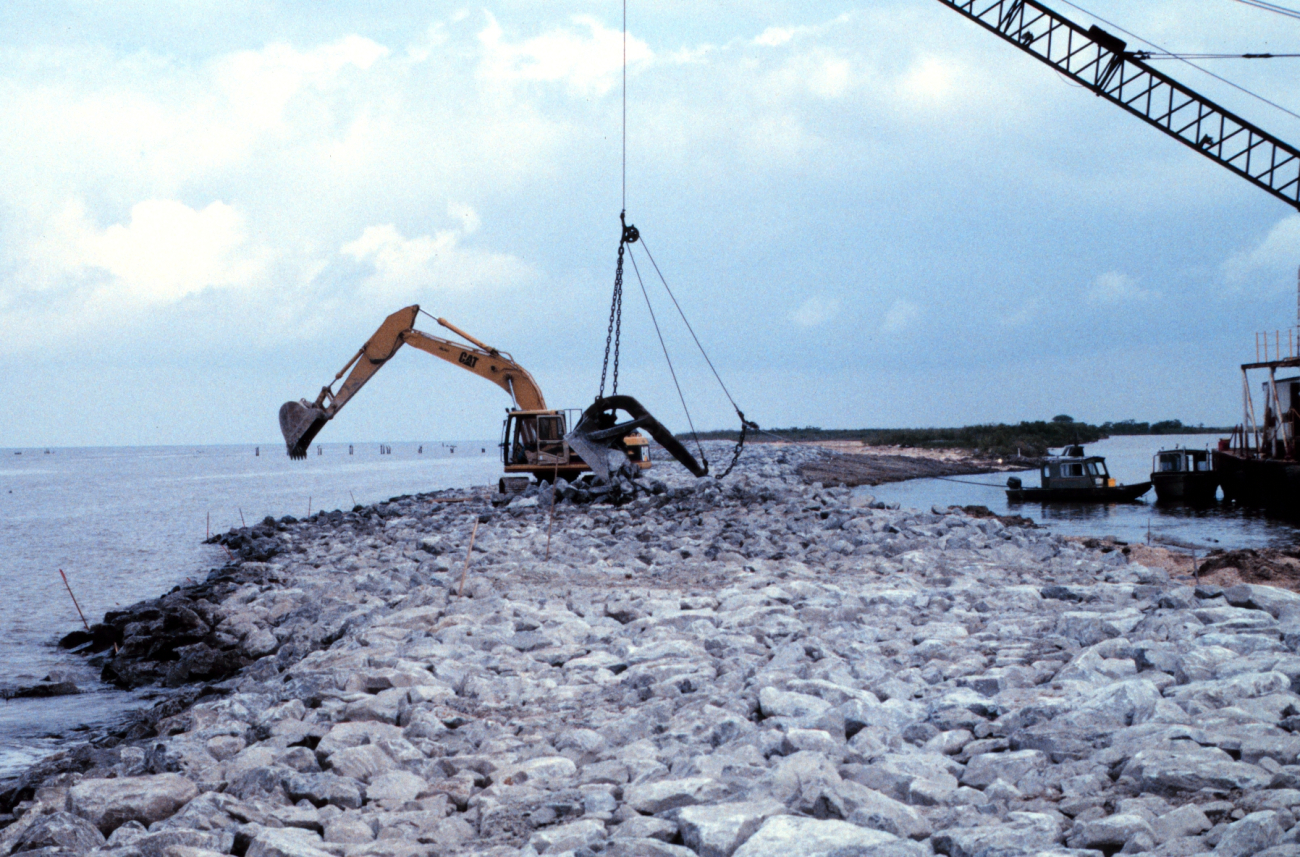 A barge-mounted crane loads rock at the construction site