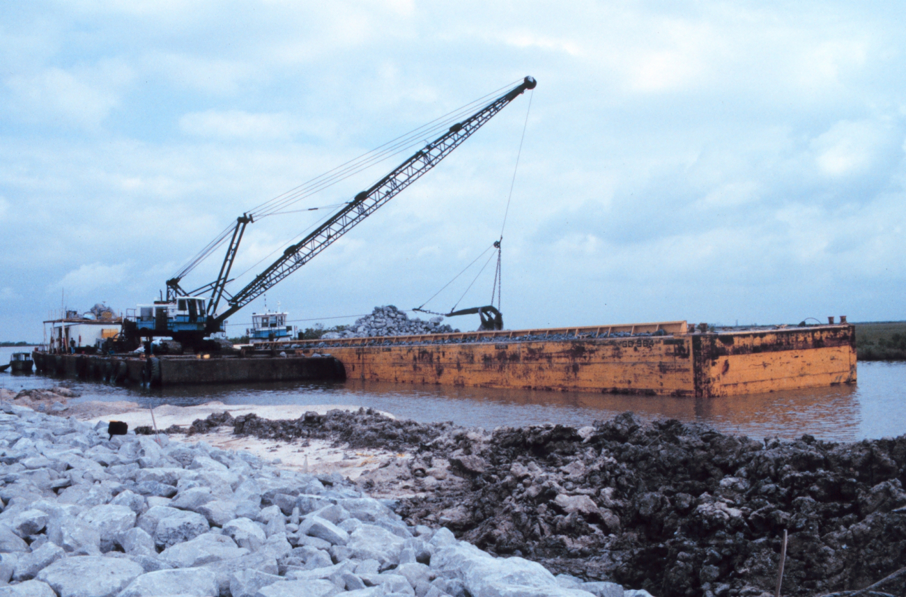A barge-mounted crane loading rock at the construction site
