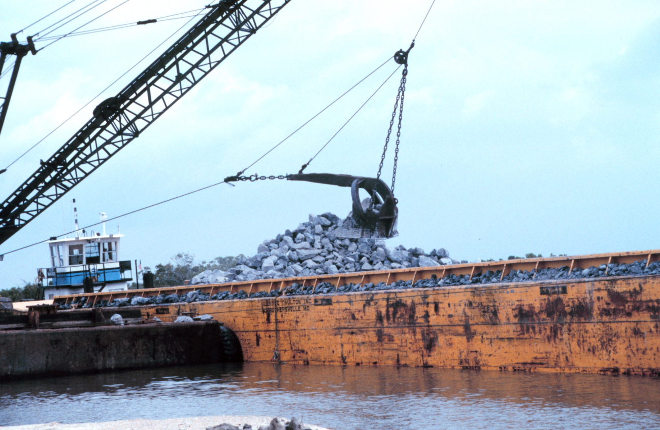 A barge mounted crane loads rock at the construction site