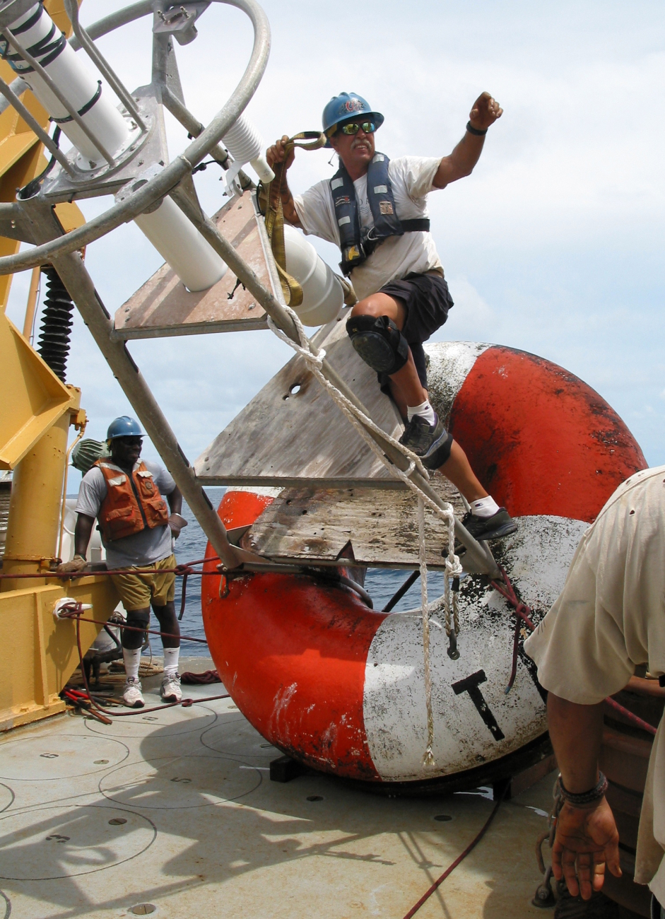 NOAA Ship KA'IMIMOANA Chief Bosun Roger Stone reaches for the cranehook so that the recovered TAO buoy can be moved off the fantail