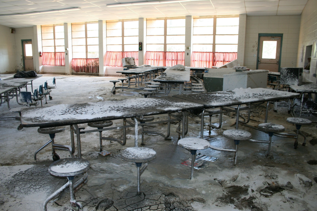 The inside of a school cafeteria with mud left on tables and stoolsafter water receded