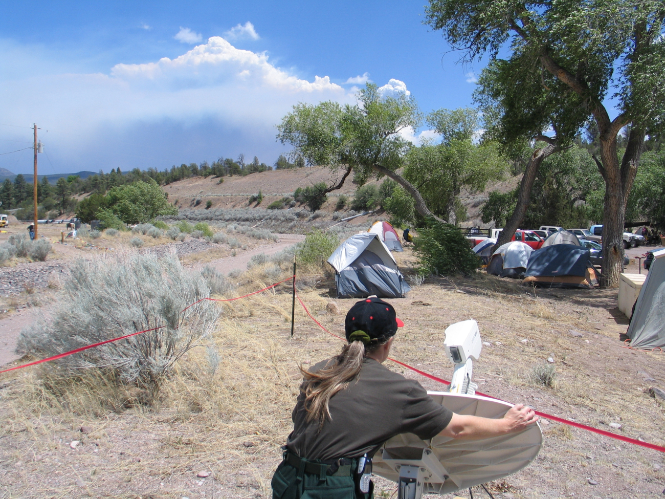 National Weather Service IMET trainee Valerie Myers positioning the Direcwaysatellite dish while smoke from the Bear Fire is seen in the distance
