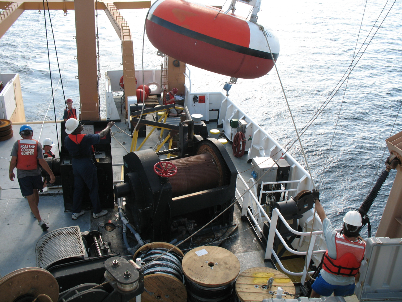 While the clouds approach and the TAO buoy streams aft with attached line,the deck crew of the NOAA Ship GORDON GUNTER move a second TAO toits pre-mooring preparation stand
