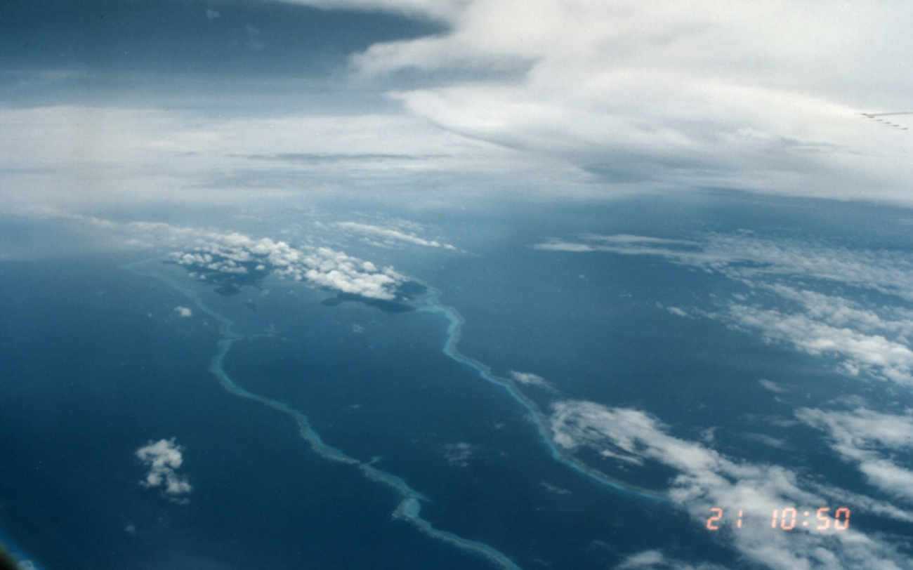 Reef seen surrounding elongate atoll with cloud streets above