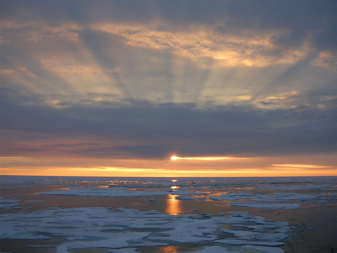 Sunset over the Arctic ice with shadow bands above and reflections on thewater below