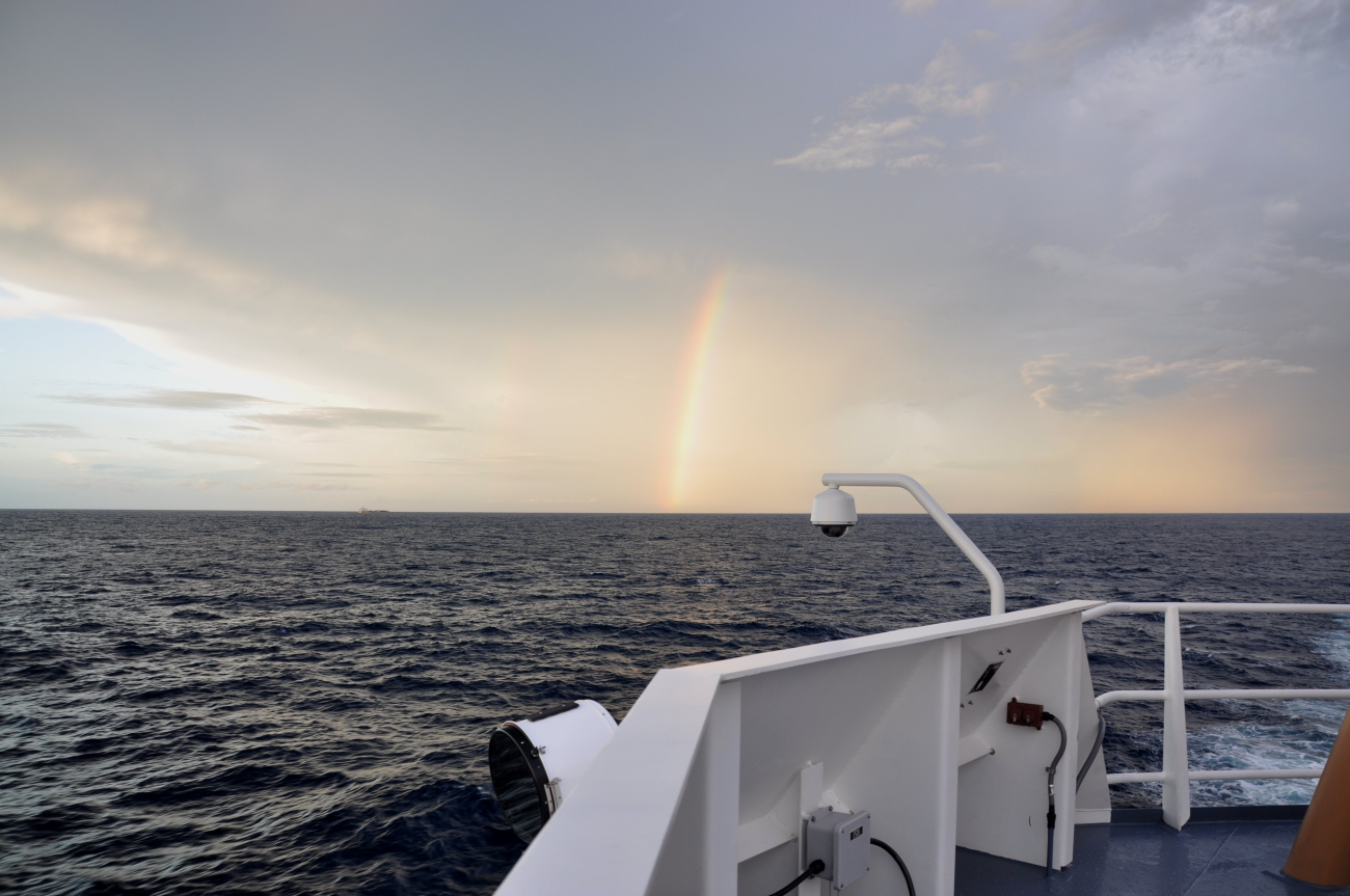 Rainbow at sunset with a small cargo ship in the distance