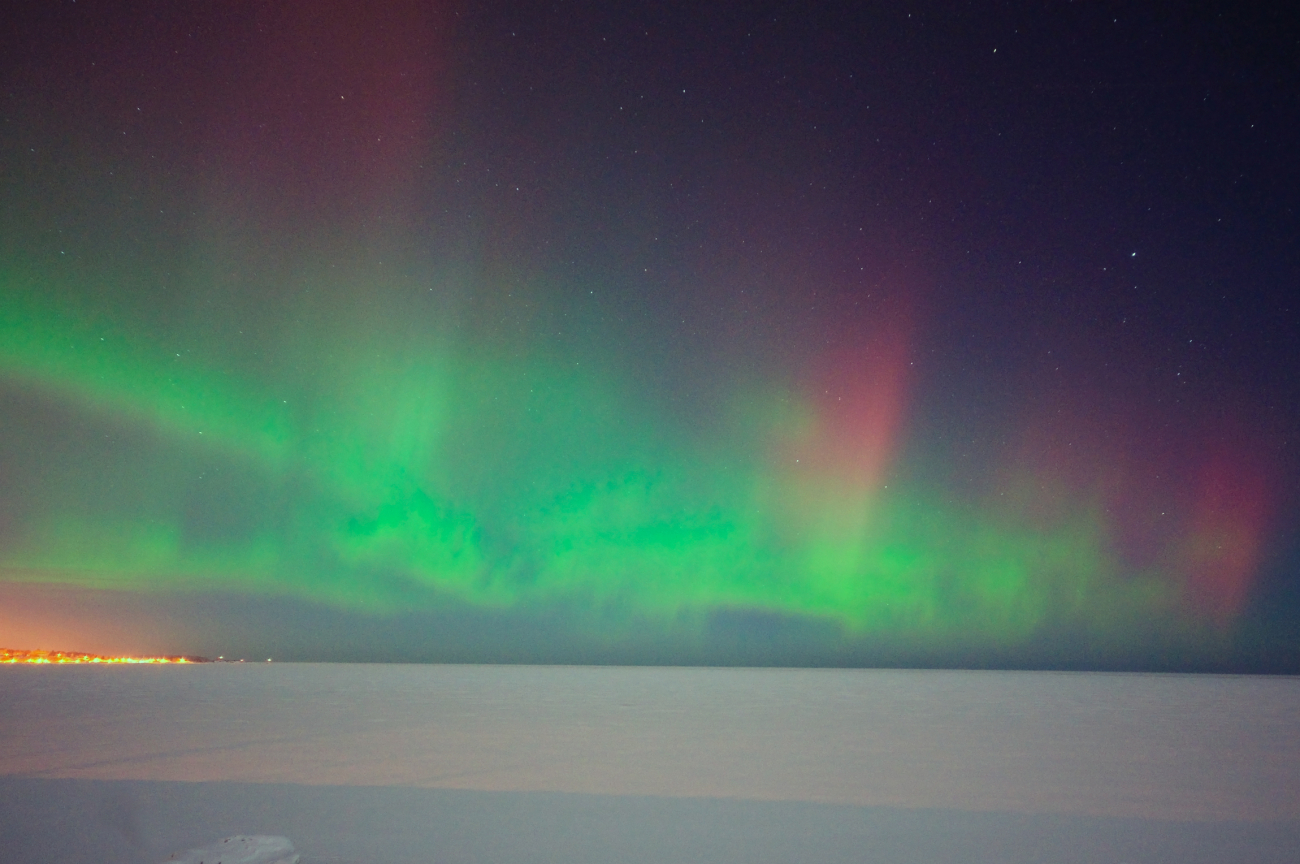 Aurora borealis over a frozen Lake Superior with the lights of Marquette on theshore