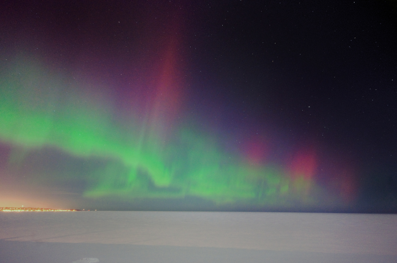Aurora borealis over a frozen Lake Superior with the lights of Marquette on theshore