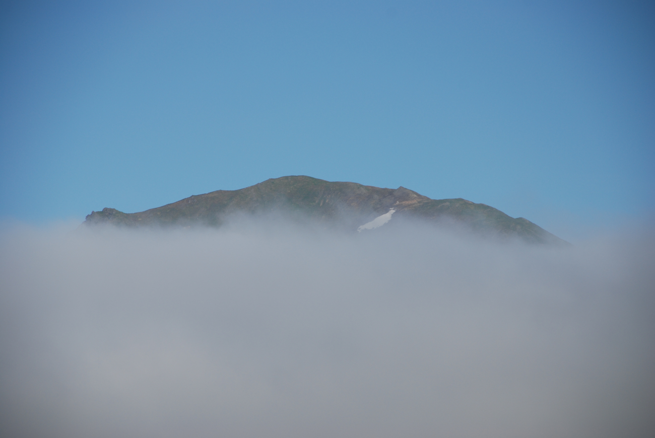 An Aleutian Island peaks its peak over the fog