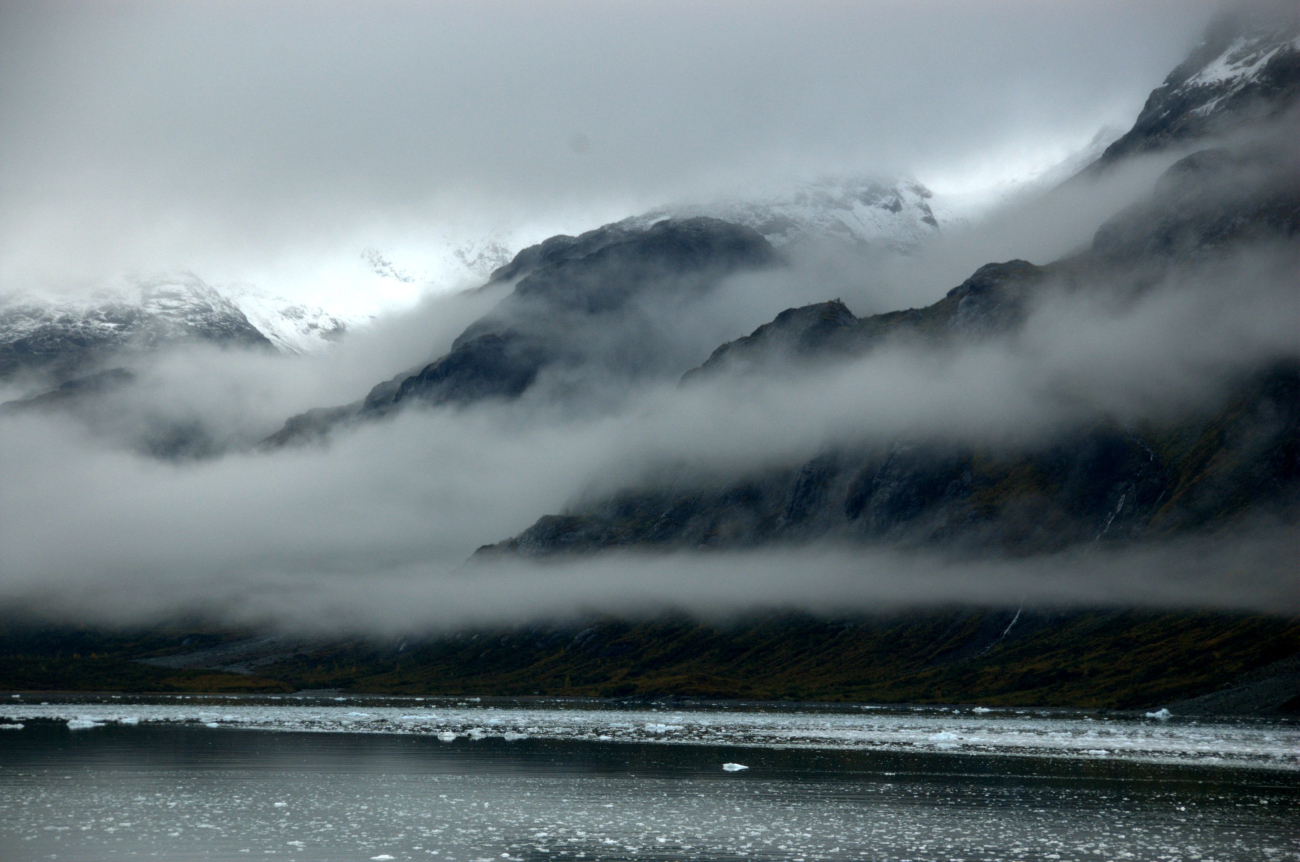 Streamers of fog fill valleys and parallel cliffs along the shore in Glacier Bay