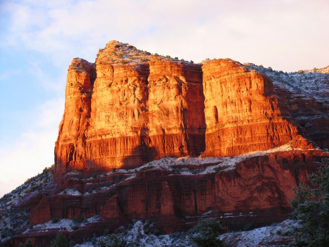 Late afternoon sun illuminates a red rock mesa with a dusting of snow