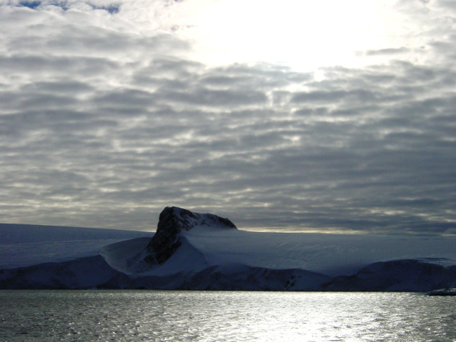 An angular mountain peak looking like the prow of a ship seemingly cuts throughan Antarctic Peninsula ice field