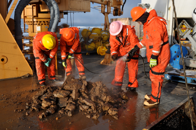 Scientists inspecting dredge haul of rocks and mud looking for benthic lifeforms