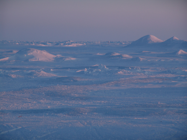 A low-angle sun illuminates hummocks on the Arctic ice