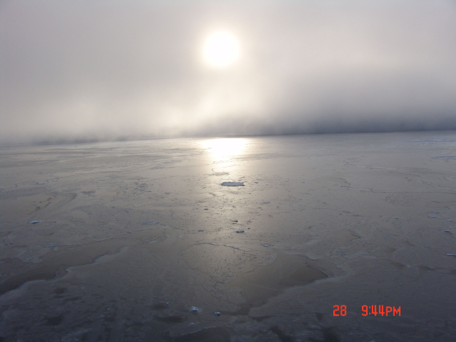Sun seen through the clouds reflecting off grey ice