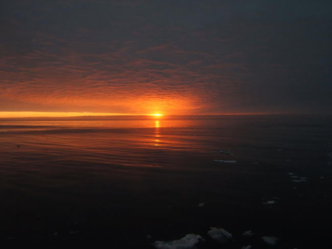 Sun, red sky, and an expanse of open water with small bits of brash ice inforeground
