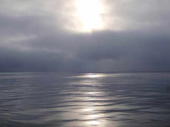 Sun seen through the clouds reflecting on grease ice