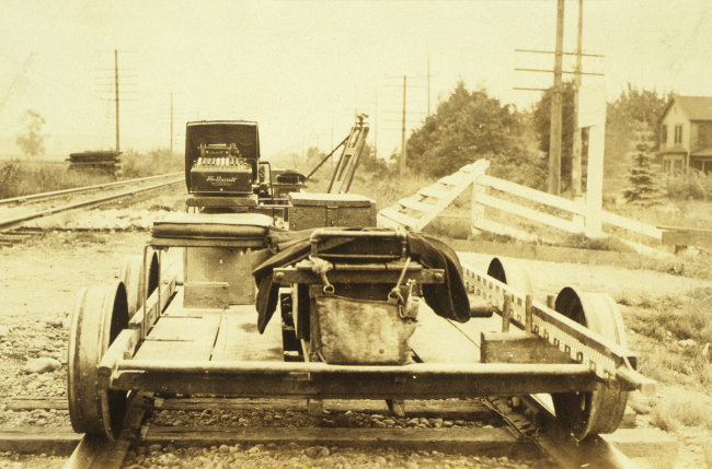 Rodman maintaining rod in vertical position over mark while steam engineapproaches