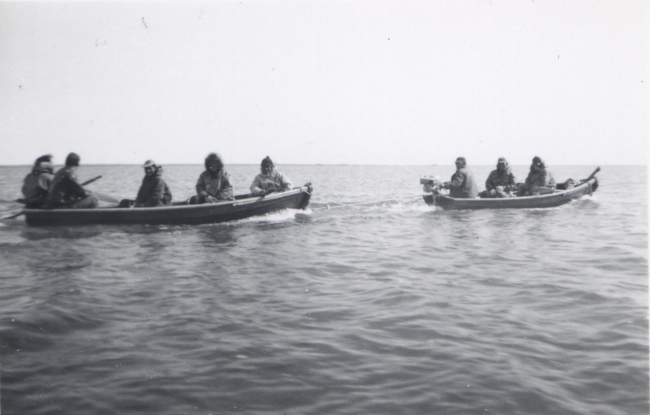 Two boats carrying native Americans - first boat equipped with outboard motortowing the second boat