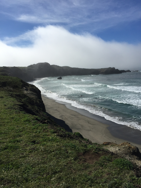 Waves of fog in the distance threaten to shroud the ocean waves along a northern California beach
