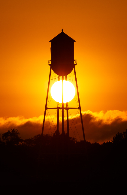 A rural Iowa watertower craddles the setting summertime sun