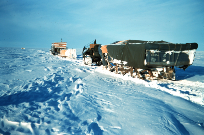 A cat train on the move across the tundraMoving equipment and supplies from Barter Island to Tigvariak IslandBlack object is a boat hull for use in the summer