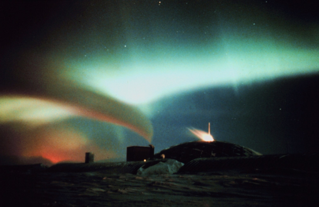 Aurora Australis - surrealistic view of South Pole station with auroral curtainand exhaust emanating in curved line fro