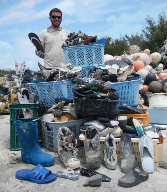 Edmund Coccagna on April 18 holds up a slipper and stands behind theother 885 slippers and rubber-soled shoes collected from the shorelines ofMidway Atoll in April 2013